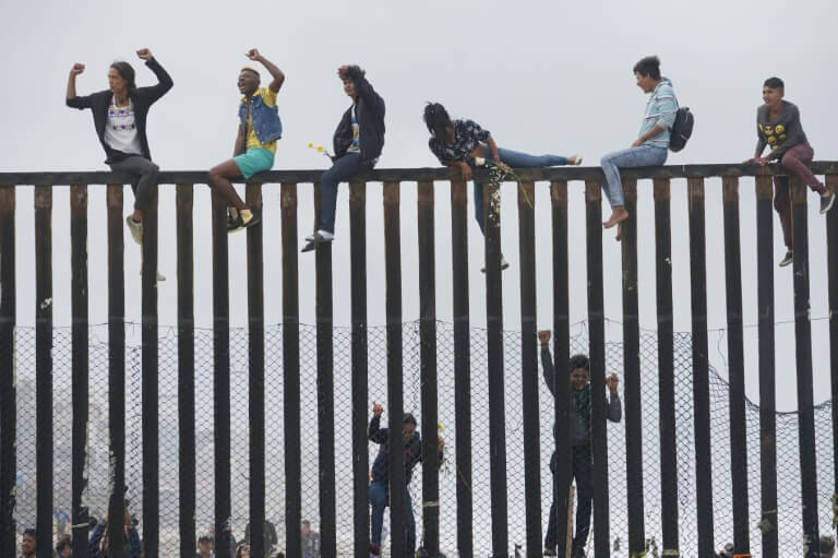 Des migrants qui ont participé à la caravane des migrants escaladent la barrière entre la frontière mexicaine 