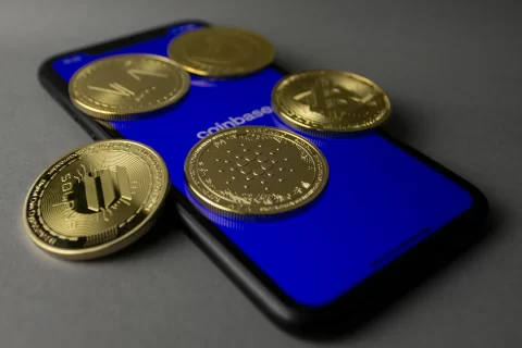 Prise de vue en studio de pièces d'or posées sur un smartphone affichant l'application Coinbase.
