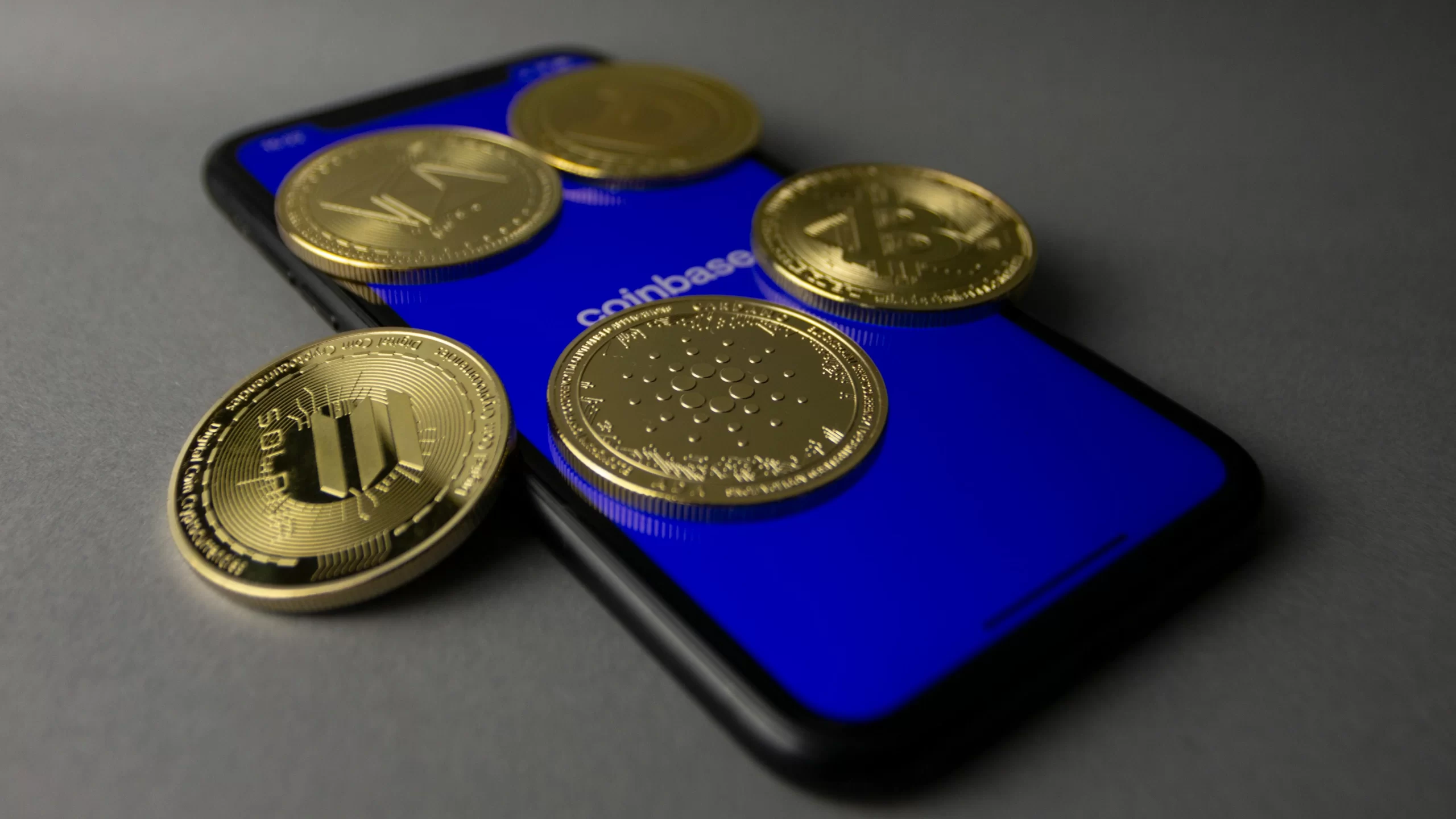 Prise de vue en studio de pièces d'or posées sur un smartphone affichant l'application Coinbase. 